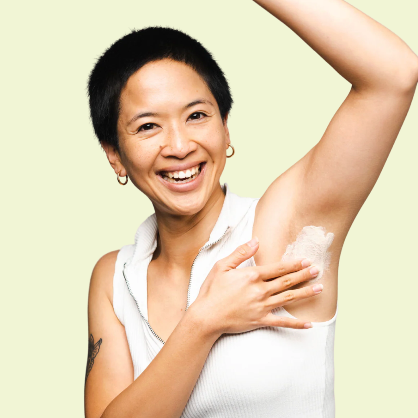 Woman applying deodorant to her armpit against a light green background