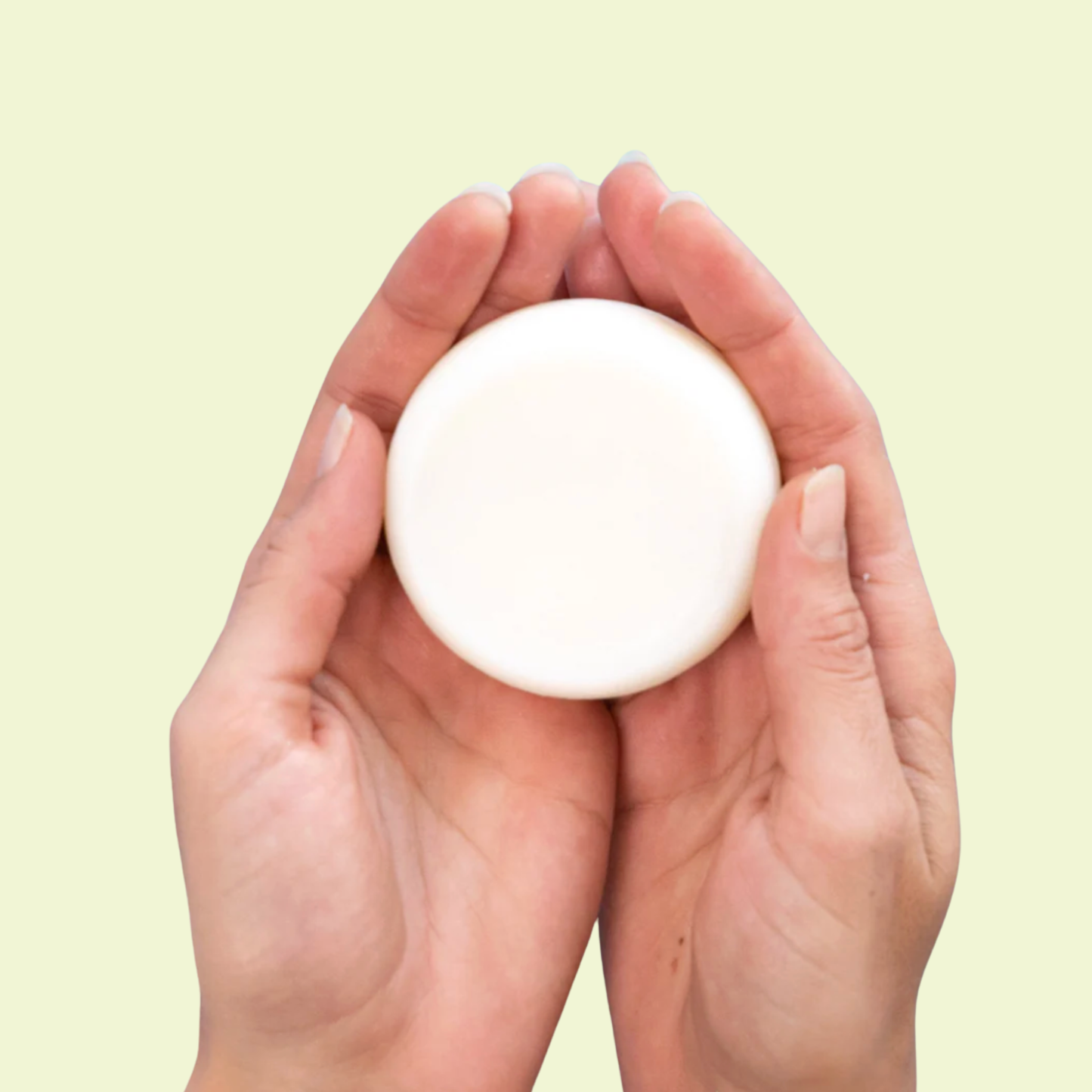 Hand holding a white round moisturiser against a light yellow background