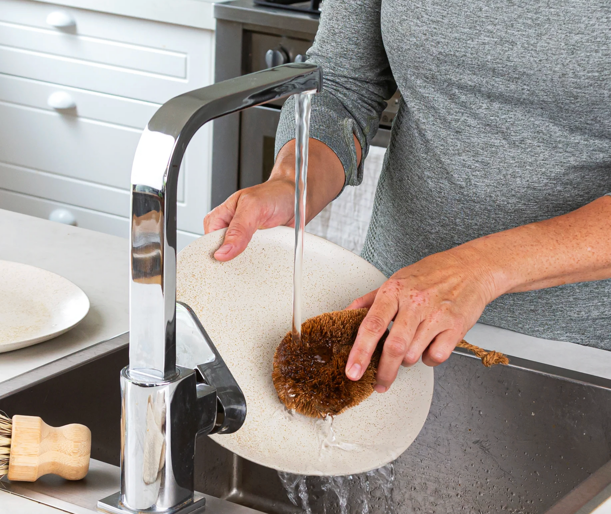 Person cleaning a kitchen sink with a scrubber under running water from a modern faucet.