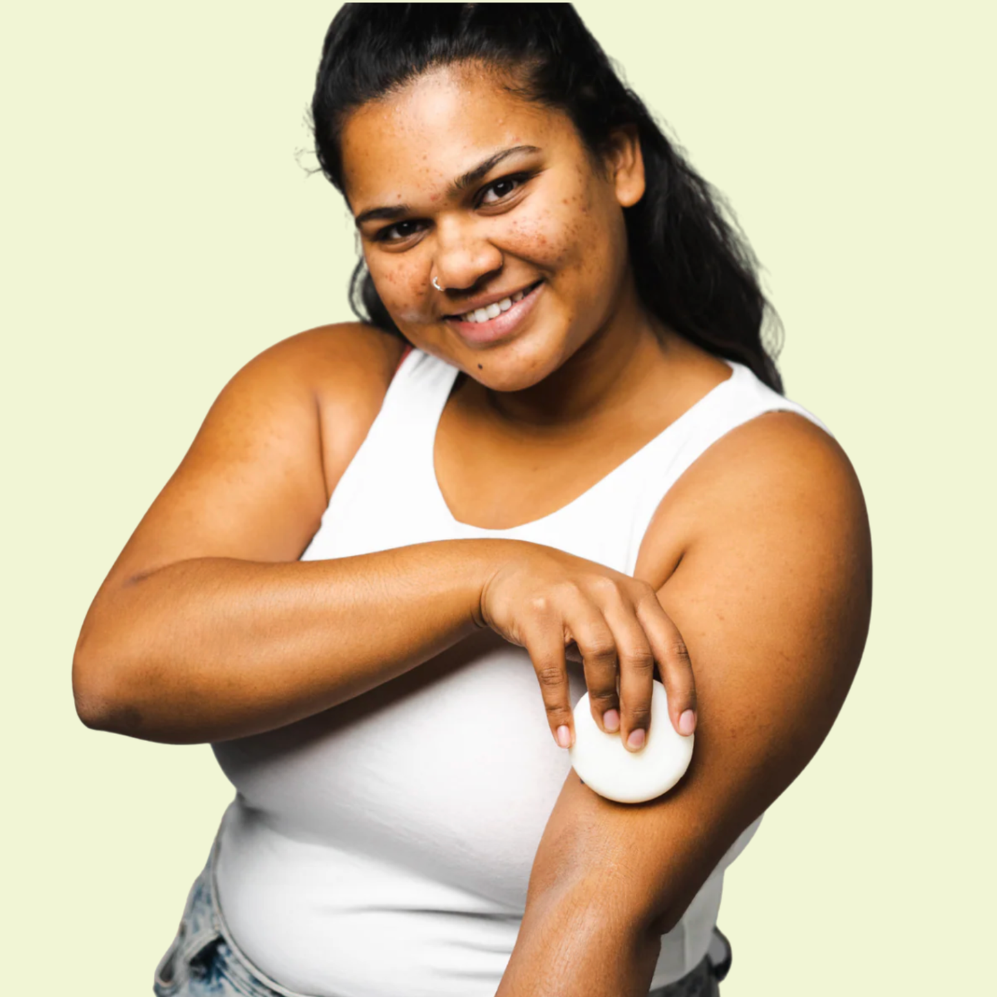 Woman applying lotion to her arm against a light green background